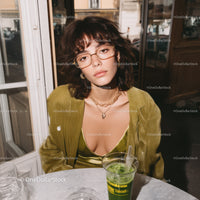 Stylish Woman in Green Dress with Glasses Sitting at a Table