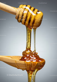 Golden honey dripping from wooden dipper to spoon