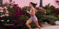 Focused young woman jogging past vibrant garden wall