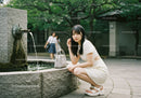 Young Woman in White Dress Relaxing by Water Fountain in Park