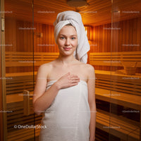 Young Woman Relaxing in Sauna with Towel Wrap and Wooden Interior