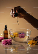 Hand Dropping Essential Oil into Water with Flowers in Glass Bowl