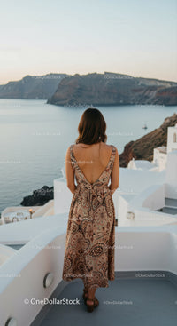 Woman in patterned dress overlooking coastal cliffs at sunset