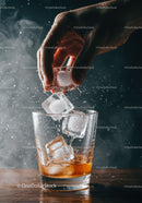 Hand Adding Ice Cubes to Glass of Whiskey on Table