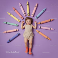 Happy toddler lying surrounded by colorful giant crayons