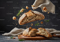 Fresh rustic bread breaking with scattered crumbs and herbs