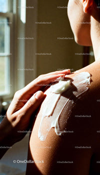 Applying moisturizing cream on sunlit shoulder skin