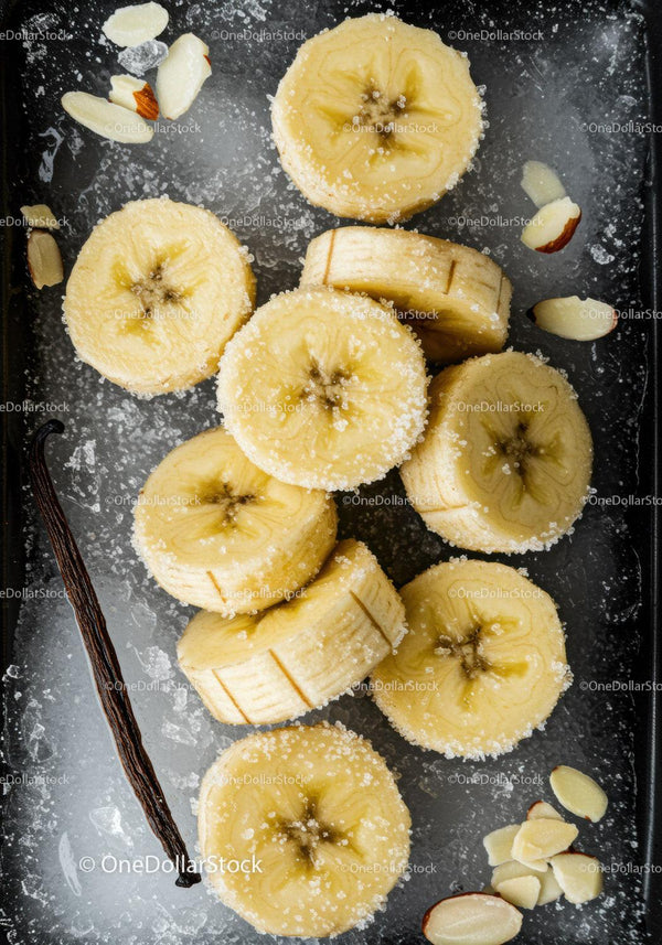 Banana slices with sugar and almond on dark surface