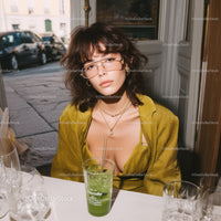Stylish Woman Wearing Yellow Blazer and Glasses Sitting with Green Cocktail