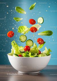 Fresh garden salad ingredients flying into white bowl