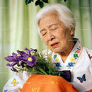 Elderly woman in traditional attire holding purple flowers