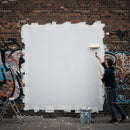 Man painting over graffiti on urban brick wall