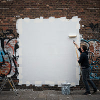 Man painting over graffiti on urban brick wall