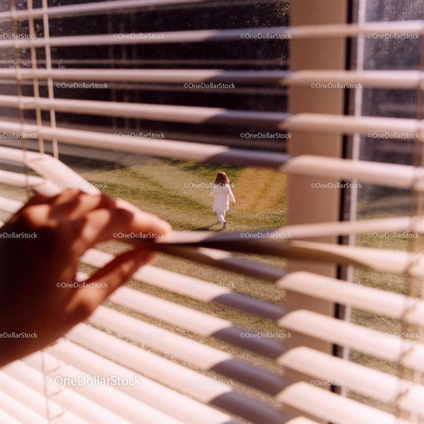 Child walking on grass viewed through window blinds