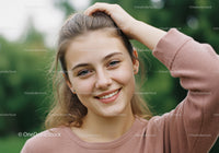 Smiling Young Woman Outdoors in Pink Sweater with Green Nature Background