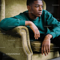 Thoughtful young man sitting on vintage olive armchair