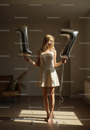 Young woman holding number balloons in sunlit room