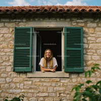 Smiling Woman by a Rustic Window with Green Shutters