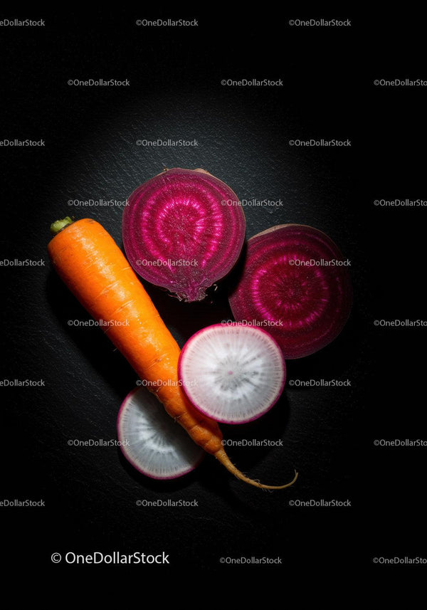 Fresh carrot with sliced beets and radish on black surface