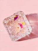 Frozen ice cube with delicate flower petals on pink