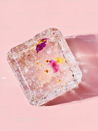 Frozen ice cube with delicate flower petals on pink