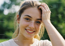 Joyful Young Woman in White T-Shirt Smiling Outdoors with Greenery