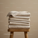Stack of folded beige textured blankets on wooden stool