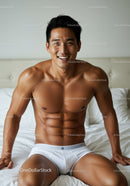 Smiling man in white underwear sitting on bed