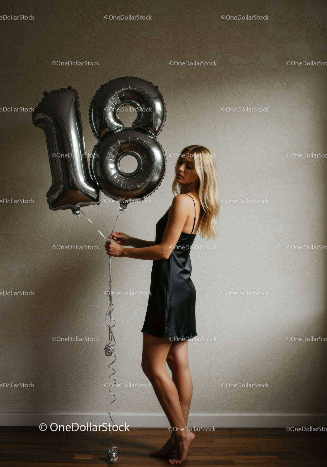 Young woman holding silver 18th birthday balloons indoors