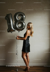 Young woman holding silver 18th birthday balloons indoors