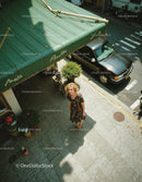 Woman in floral dress standing on city sidewalk near parked car and bicycle