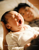 Yawning newborn in parent’s gentle embrace at home