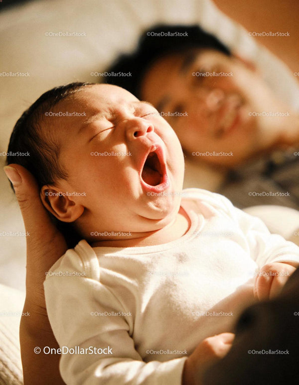 Yawning newborn in parent’s gentle embrace at home