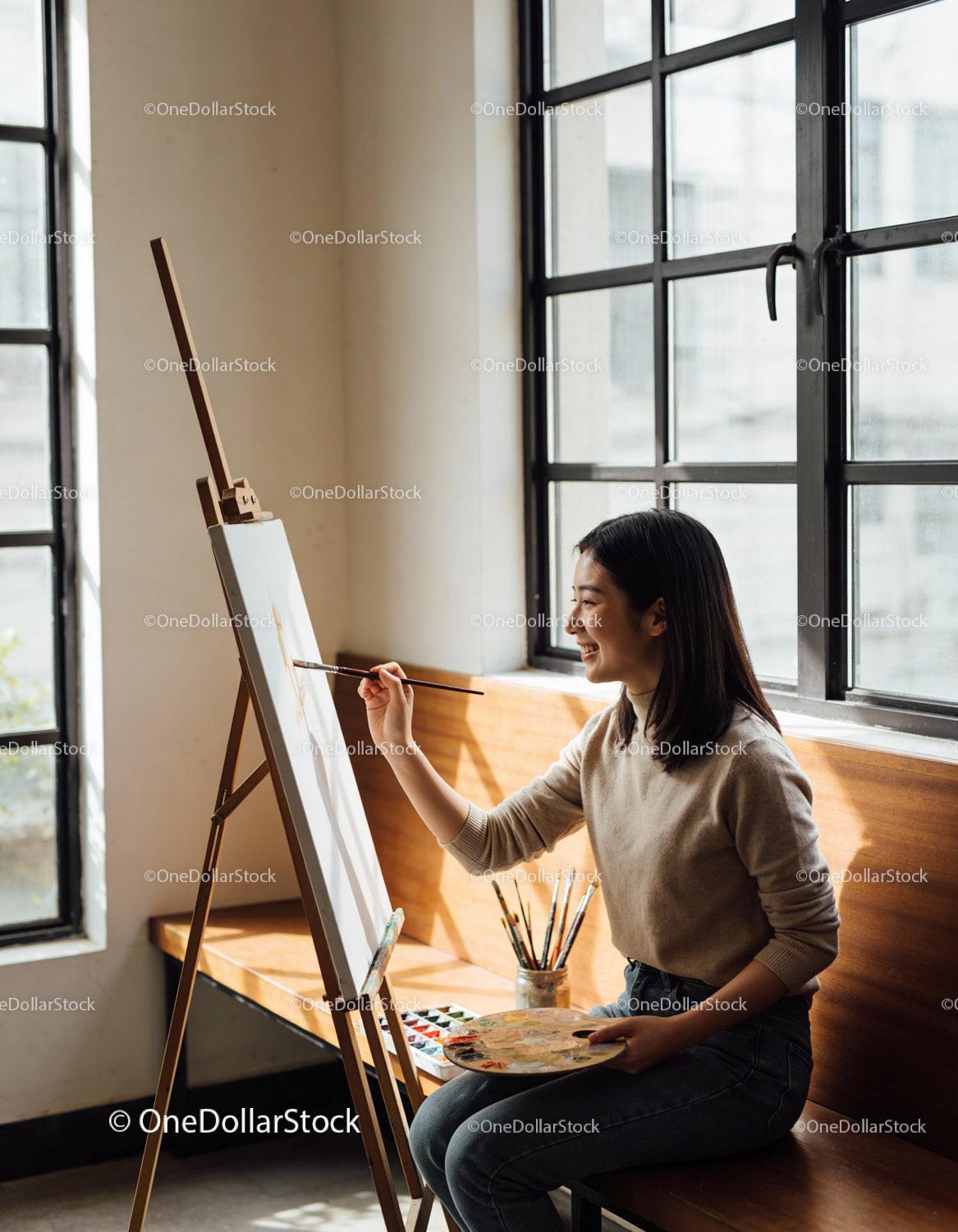 Young woman enjoying painting by large window light