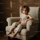 Toddler sitting thoughtfully on cozy armchair indoors