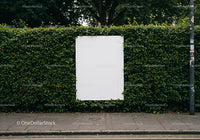 Blank white poster on lush green hedgerow by street