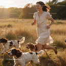 Young woman joyfully running with spaniels in golden field
