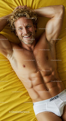 Smiling man relaxing on yellow bed in white briefs
