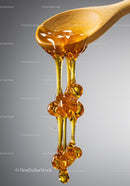 Golden honey dripping from wooden spoon closeup