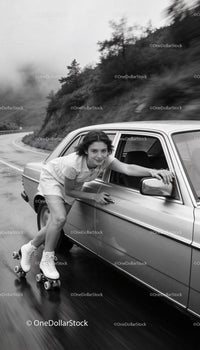 Young Woman Roller Skating Alongside Car on Curvy Road