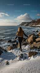 Woman walking on snowy rocky shore by ocean cliffs