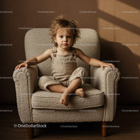 Serious toddler sitting cross legged on cozy armchair