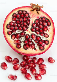 Fresh pomegranate half with scattered seeds on white background