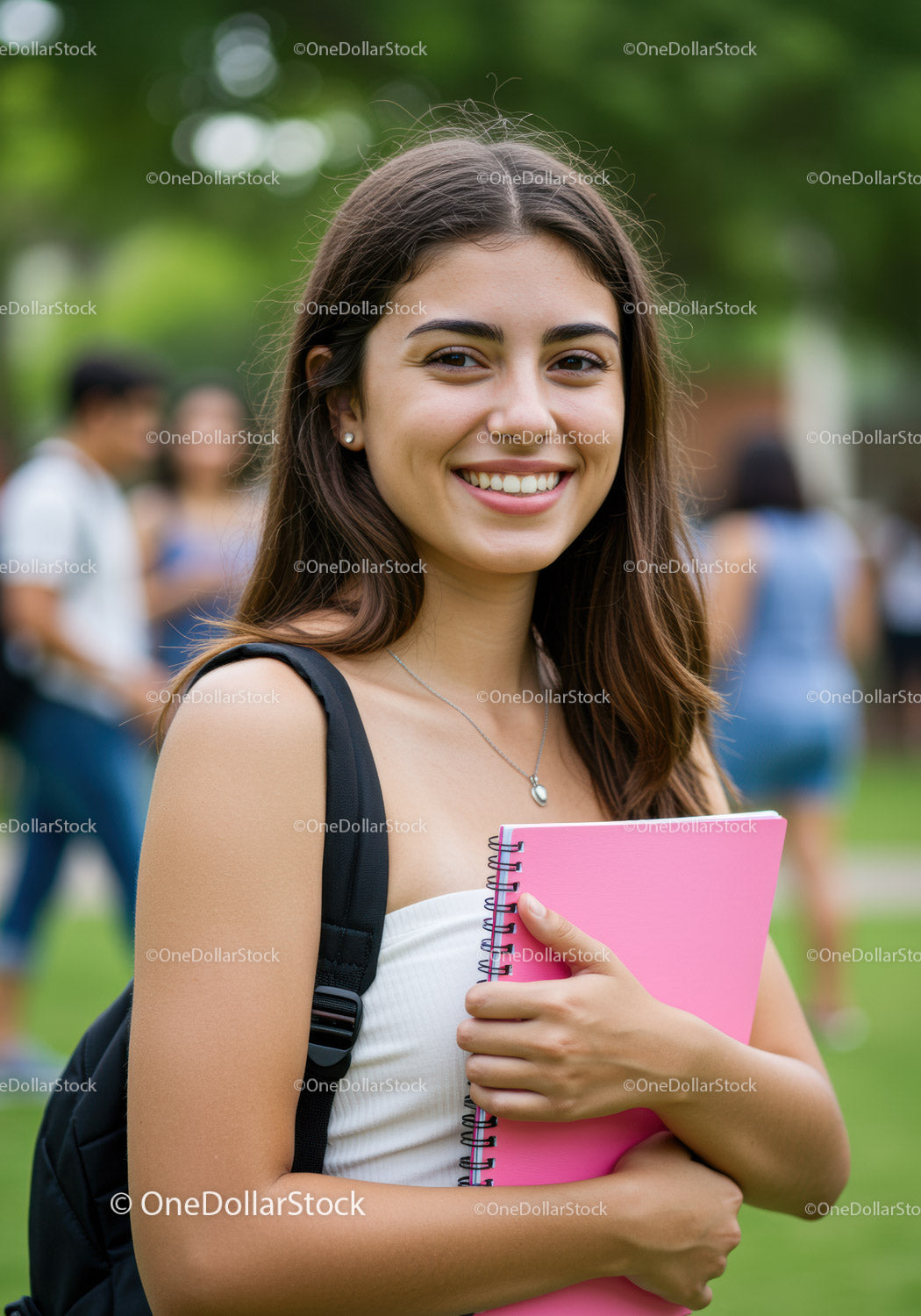 Szczęśliwa młoda studentka trzymająca różowy notes na zewnątrz