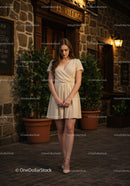 Fashionable Young Woman in Beige Dress Walking on City Street at Night