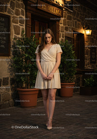 Fashionable Young Woman in Beige Dress Walking on City Street at Night