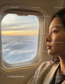 Young Woman Gazing Through Plane Window at Sunset Clouds