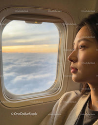 Young Woman Gazing Through Plane Window at Sunset Clouds