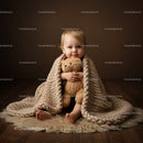 Toddler wrapped in knitted blanket hugging teddy bear