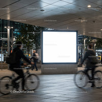 Urban night scene with illuminated blank billboard and cyclists